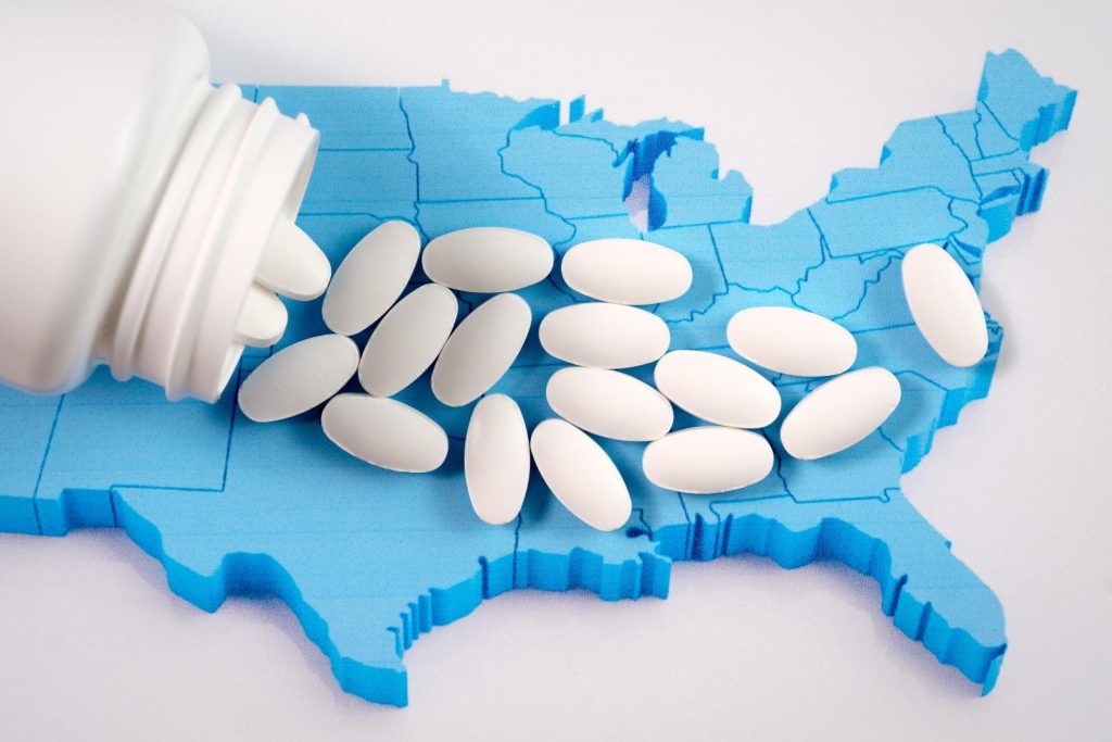 White pills spilled on top of a blue outline of the United States