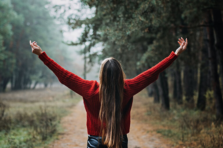 Woman in the middle of the woods with her arms up 

