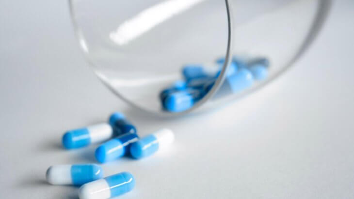 Blue and white pills spilling out of a glass onto a table