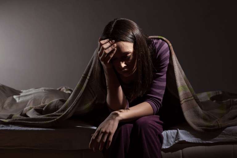 A woman in a dark bedroom holds her head in distress
