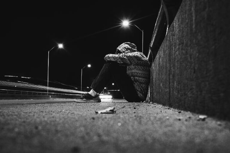 Man in hooded jacket sitting on the street at night.