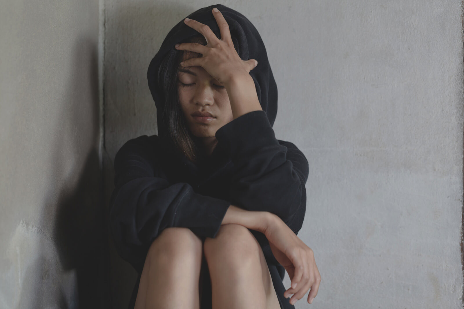 Woman wearing a black hoodie sitting against a wall