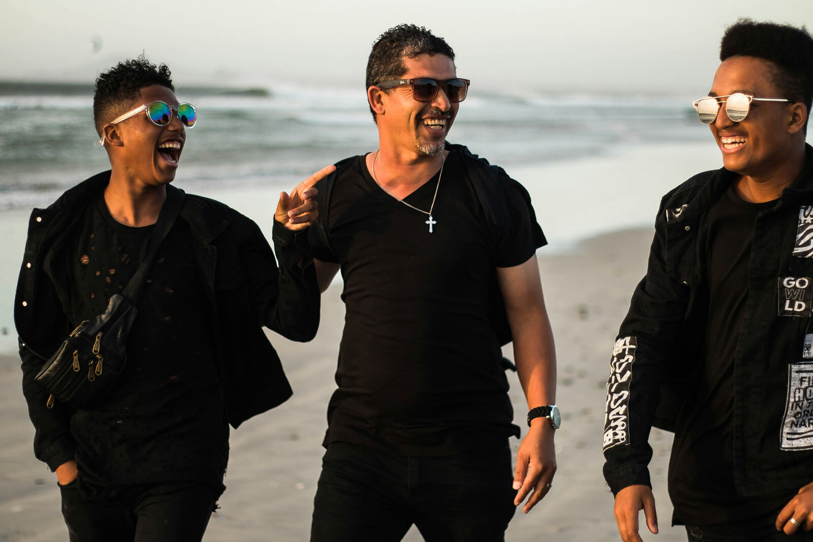 Three men laughing and walking together on the beach