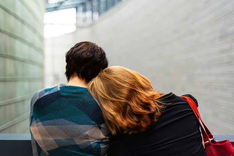 A redheaded woman resting her head on a friend’s shoulder