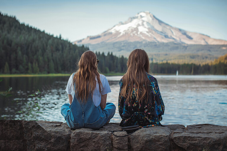 Two women sitting on a stone wall looking out at a lake