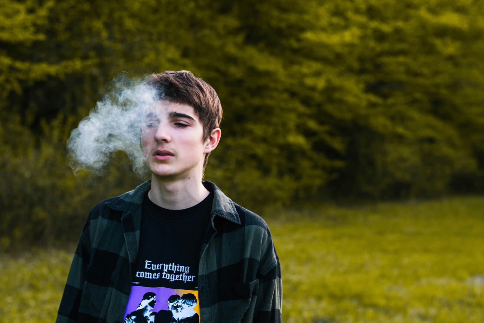 A young man in a graphic T-shirt exhaling a cloud of smoke