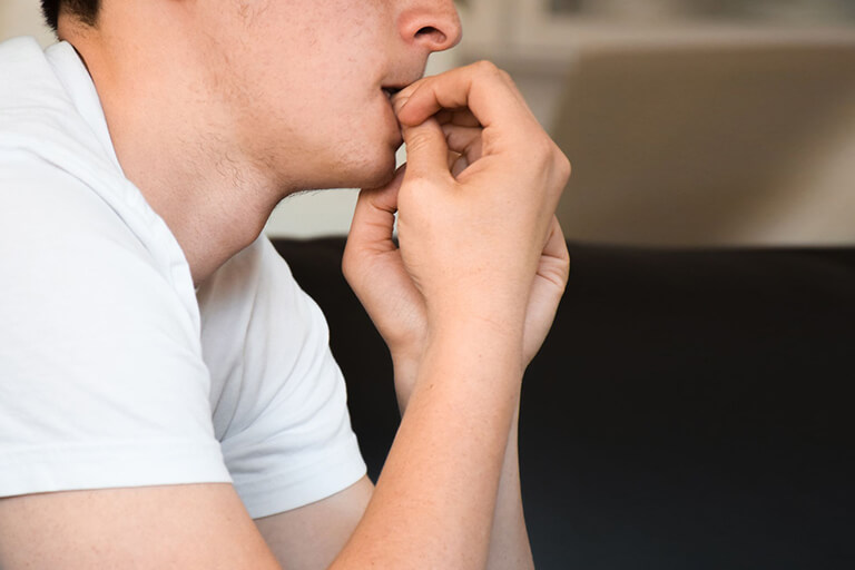 A man in a white T-shirt nervously bites his nails