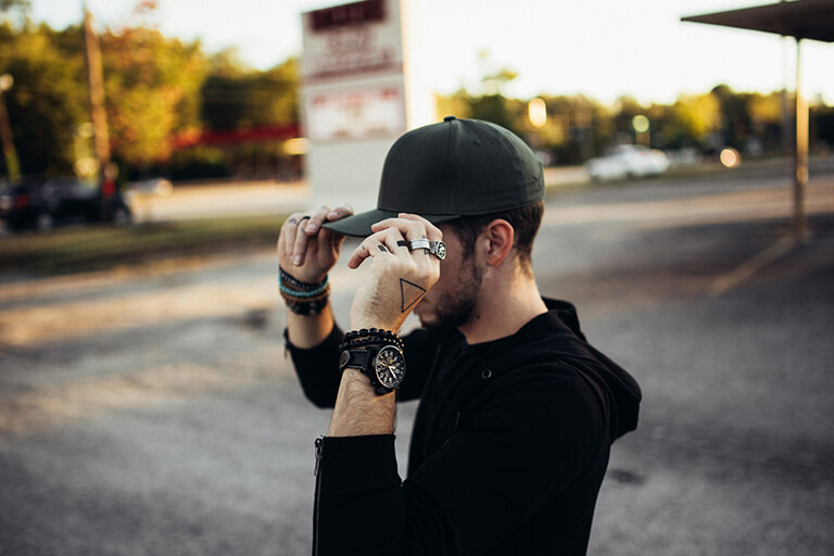 A man with a black baseball cap and accessories in a parking lot