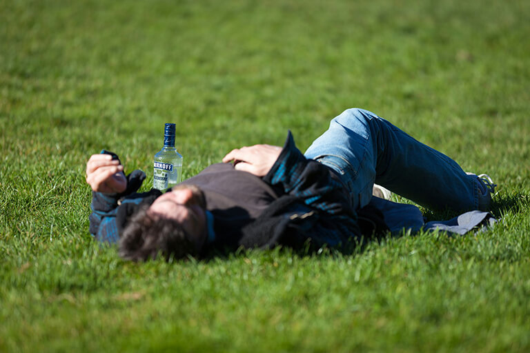 A man lying unconscious on a grassy field with a bottle of vodka next to him