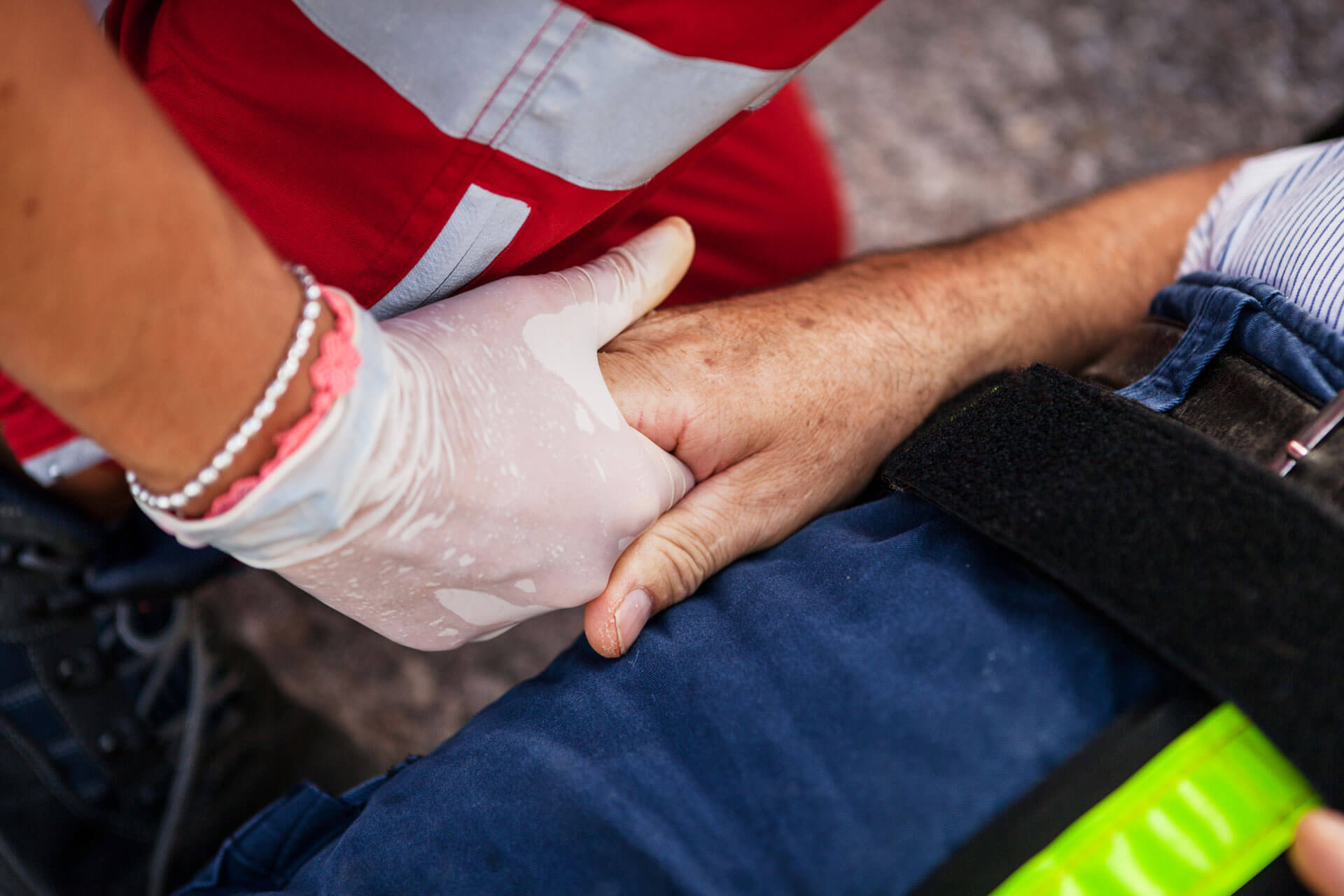A first responder wearing a latex glove holds the hand of someone receiving medical assistance
