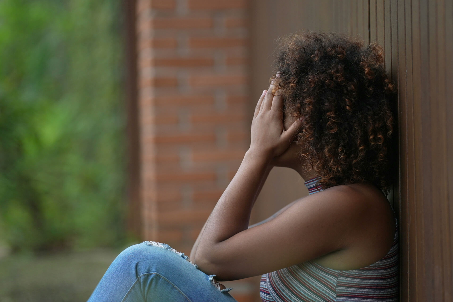 A woman sits against a wall with her head in her hands