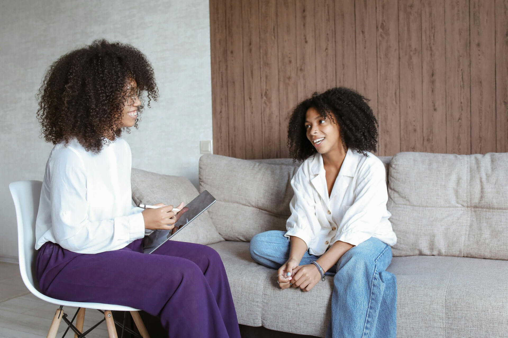 A female therapist sits across from a client during a therapy session, both smiling.
