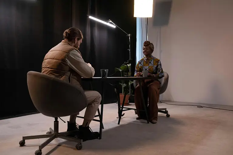 A man and a woman sit at a desk recording a podcast. 
