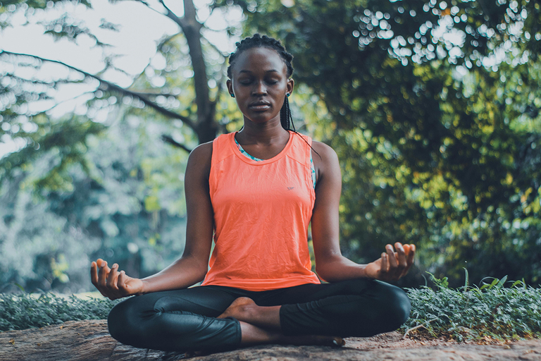 A woman meditates outdoors with her legs crossed and eyes closed.