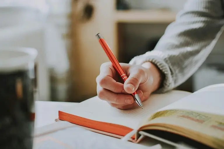 A man writes in a journal with a red pen. 