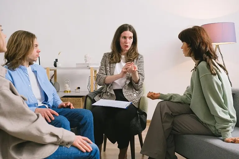 A therapist speaks to two women and a man during a group therapy session.