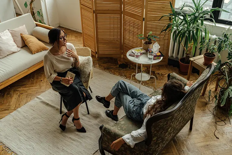 A woman sitting on an armchair opposite another woman during a therapy session.