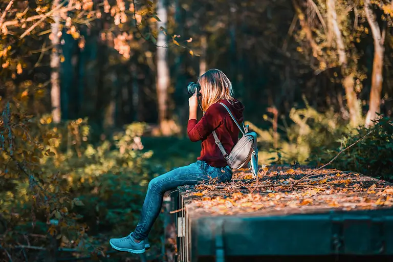 A woman wearing a backpack taking pictures of autumn scenery with a camera.