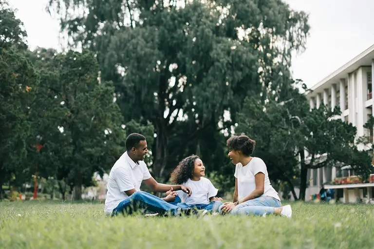 Family relaxing together on grass in a park, smiling and connecting.
