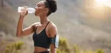 While jogging through nature, a woman pauses to take a refreshing sip from her water bottle, reflecting on summer self-care ideas.