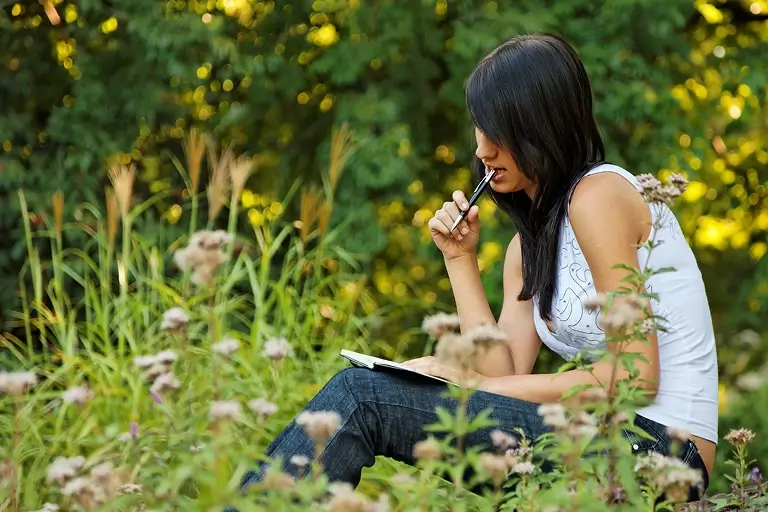 A woman sits in a field and journals.