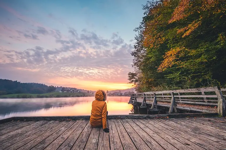An individual sits in a serene waterfront setting, watching the sunset from a dock.